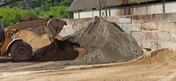Radlader schüttet Material vor einer Betonblocksteinwand an, das Haufwerk liegt einseitig an der Wand