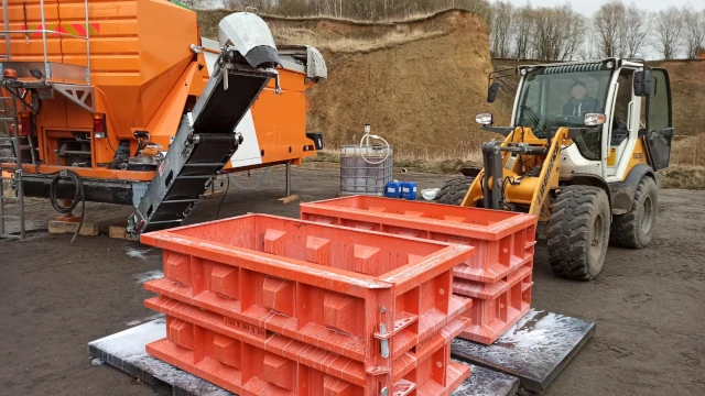 Mobile Mischanlage und gestapelte Schalungen für Betonblocksteine, daneben ein Radlader